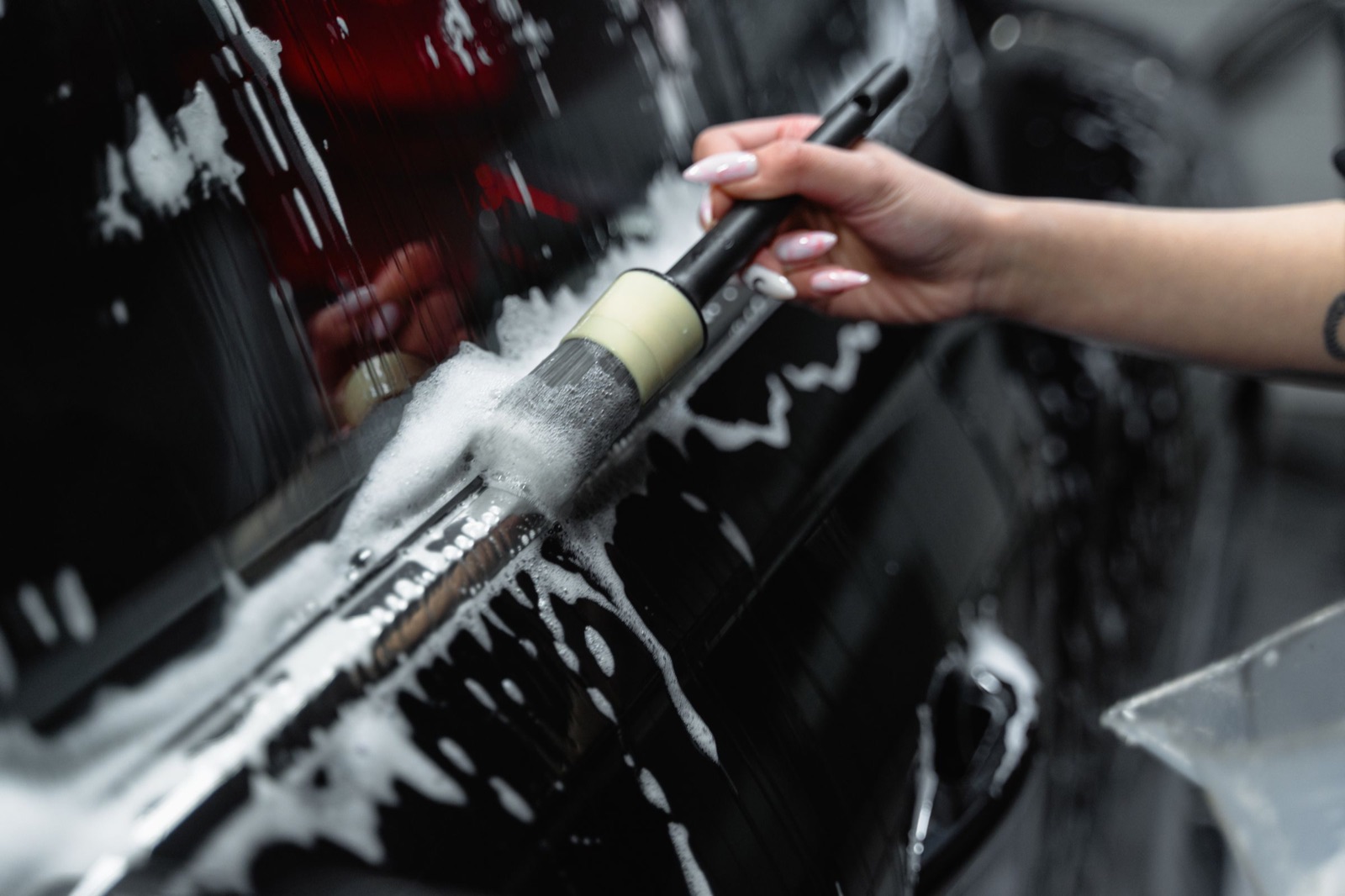 A detailing brush cleaning the exterior of a dark car